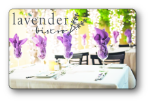 Lavender logo, over tables with white table clothes with lavender colored cloth napkins tucked inside wine glasses inside the